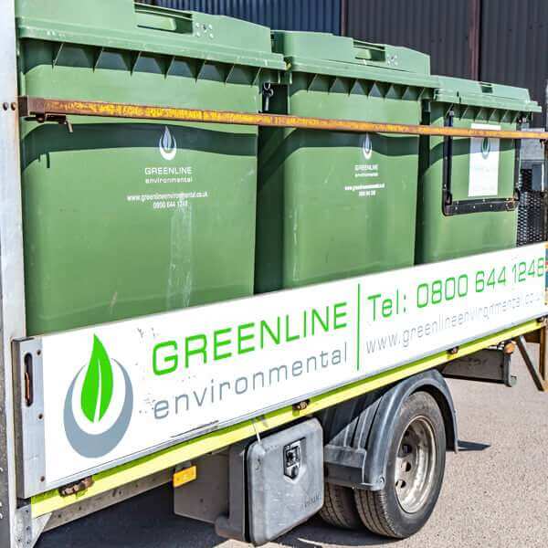 A man with safety glasses and a yellow vest observes a garbage bin, highlighting his role in waste management.