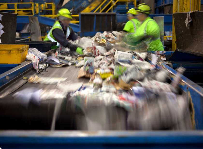 A man with safety glasses and a yellow vest observes a garbage bin, highlighting his role in waste management.